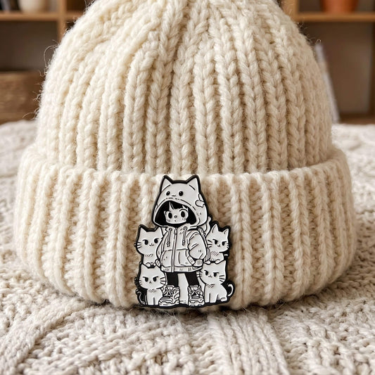 Detailaufnahme eines 18mm Druckknopf KLIQs mit schwarz-weißem Emaille-Motiv: Ein Anime Hoodie-Mädchen umringt von süßen Neko-Katzen. Der hochwertige KLIQ ist als stylisches Accessoire an einer weißen Strickmütze befestigt und zeigt den modernen Kawaii-Look im Klicksystem.