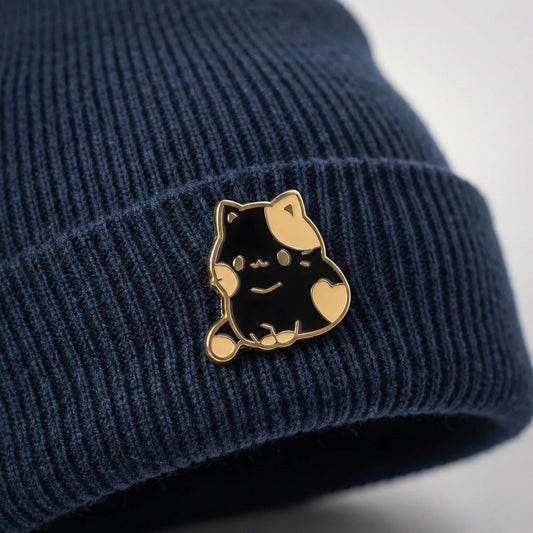 Anwendungsbeispiel eines 18mm Mochi Cat Emaille Motiv-KLIQs auf einer blauen Beanie-Mütze. Das Bild zeigt, wie der niedliche Katzen-Druckknopf KLIQ als Accessoire an der Kleidung wirkt und der Mütze einen individuellen Look verleiht.