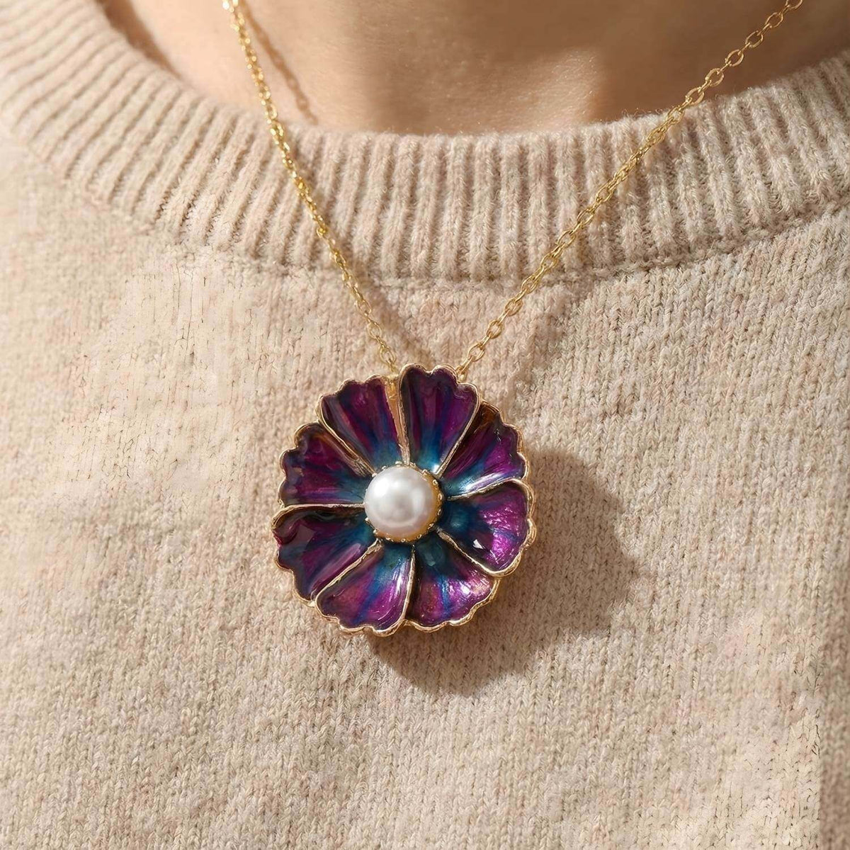 Nahaufnahme der lila-blauen Blüte "Mystic Violet" als Anhänger einer goldenen Kette. Die 18mm Blüte mit Perle liegt auf einem beigen Strickpullover. Zeigt das Produkt als Halsschmuck.