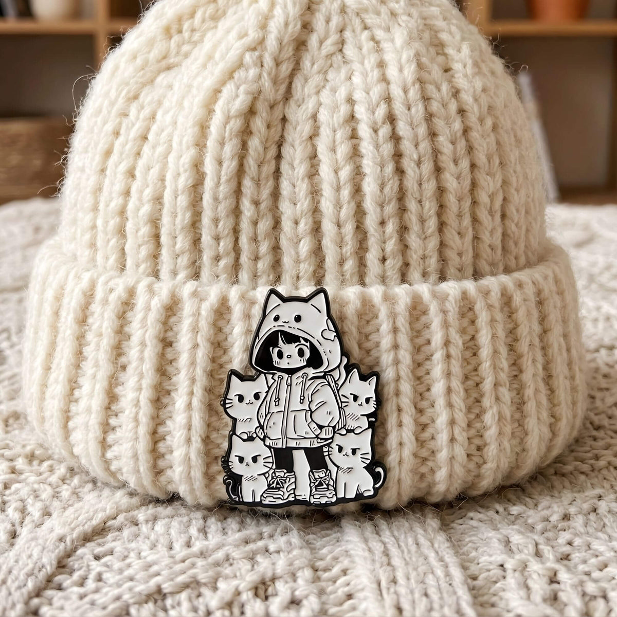 Detailaufnahme eines 18mm Druckknopf KLIQs mit schwarz-weißem Emaille-Motiv: Ein Anime Hoodie-Mädchen umringt von süßen Neko-Katzen. Der hochwertige KLIQ ist als stylisches Accessoire an einer weißen Strickmütze befestigt und zeigt den modernen Kawaii-Look im Klicksystem.
